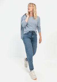 Gestreepte blauwe en witte casual top met middelange mouwen, gecombineerd met high-waisted denim jeans en lichtgekleurde sneakers.