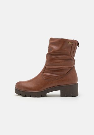 Botín de cuero marrón con diseño arrugado, puntera redondeada y suela gruesa. Presenta un zipper lateral y acentos texturizados.