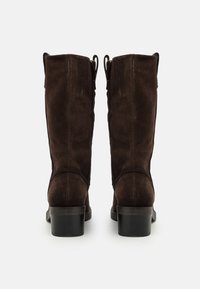 Botas de ante marrón hasta la rodilla con punta redondeada, tacón cuadrado y dos lengüetas en la parte superior para facilitar su colocación. Textura suave con un ligero brillo.