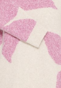 Pull léger avec une base crème ornée de grands motifs abstraits roses, en tissu de laine texturé, avec des poignets côtelés.