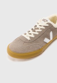 Bež tenisica od antilopa sa kremasti vezicama i postavom, gumenim đonom i bijelim logom. Imaš ušivene detalje i uzorak teksturiranog đona.