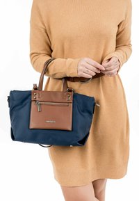 Borsa a mano blu navy con dettagli marroni, tasca con zip e accessori metallici. Texture liscia e forma strutturata. Design compatto e funzionale.