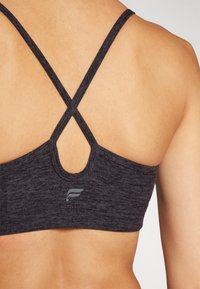 Juoda sportinė liemenėlė su kryžminiais dirželiais nugaroje, turi apvalią išpjovą ir mažą logotipą prie apačios. Lygi tekstūra.
