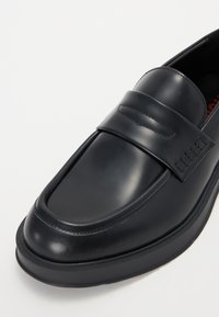 Juodų odinių loafers su lygiu paviršiumi, su akcentuota juosta viršuje ir tekstūruota padais, užtikrinančiu geresnį sukibimą.