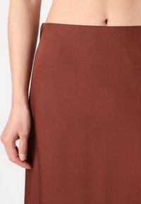 Brun midi skjørt laget av glatt stoff, med en tilpasset midje og rett silhuett. Teksturen ser myk ut med minimale detaljer.