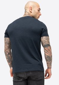 Navyblaue Baumwoll-T-Shirt mit kurzen Ärmeln, Rundhalsausschnitt und subtiler Textur. Mit einem kleinen Logo-Tag am Saum.