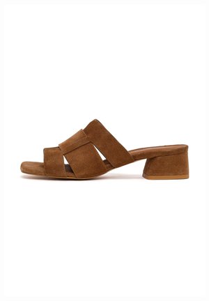 Brauner Wildleder-Open-Toe-Mule mit breiten gekreuzten Riemen und niedrigem Blockabsatz auf weißem Hintergrund.