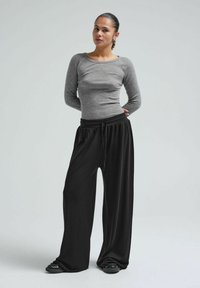 Graues Langarmshirt mit rundem Halsausschnitt, kombiniert mit schwarzen, locker sitzenden Jogginghosen mit Kordelzug und schwarzen Slippern.