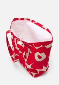 Sac en tissu rouge avec un grand motif floral beige, ouvert en haut, deux poignées et une doublure intérieure lisse. Design robuste sans éléments métalliques.