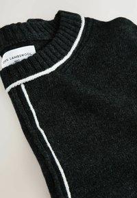 Maglione nero in 100% lana d'agnello con colletto a coste e una linea bianca lungo la cucitura della spalla. Texture morbida, ripiegato.