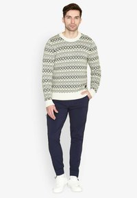 Strikket sweater i creme med sorte geometriske mønstre, parret med navy bukser og hvide sneakers. Har ribbet manchetter og kant.