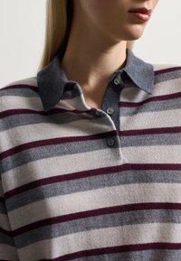 Camisa polo de rayas en tela suave que presenta rayas en gris, gris claro y marrón; cuello gris con dos botones en el escote.