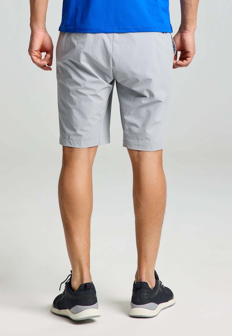 Shorts gris avec une finition matte et légère ; longueur genou avec une coupe décontractée. Associés à des chaussures de sport noires avec des semelles blanches.