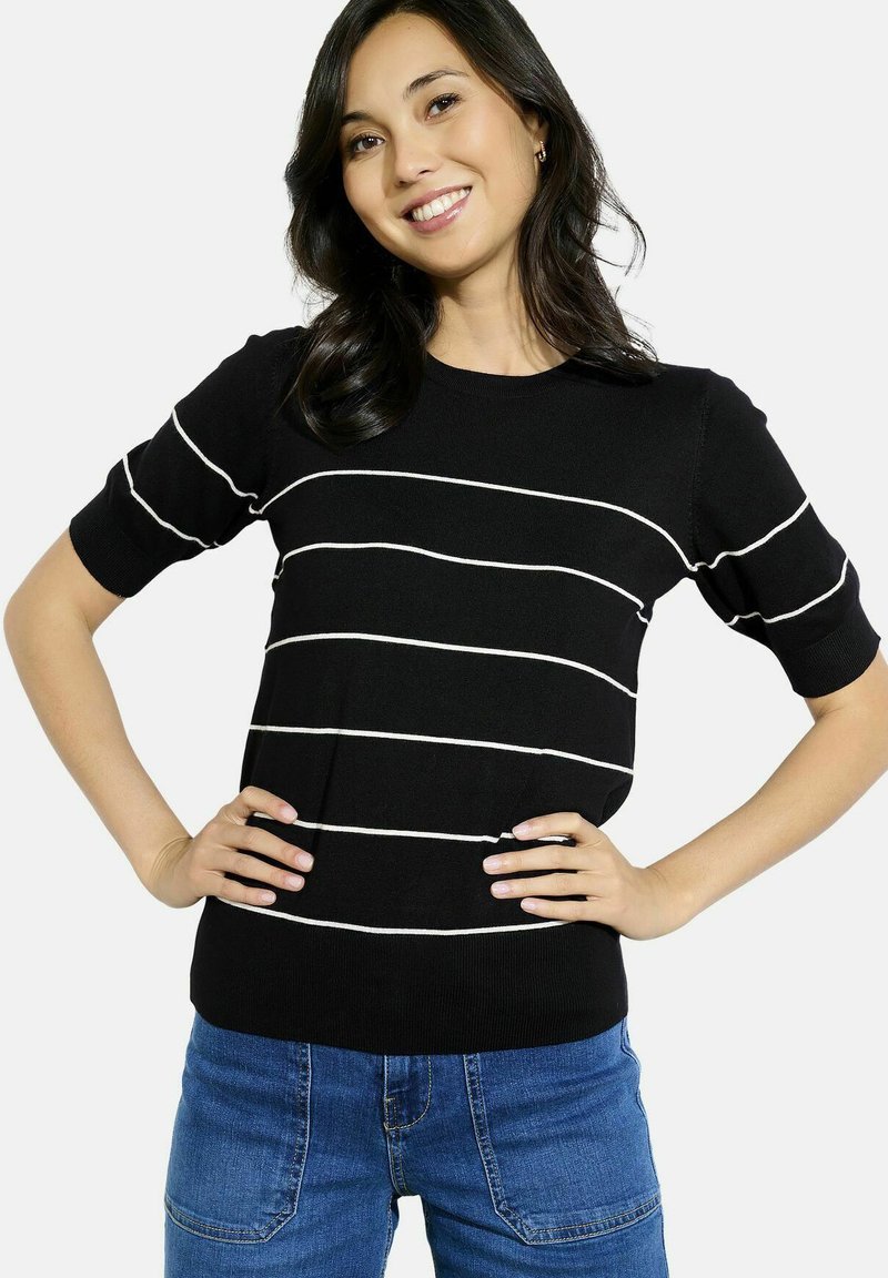 Pull en maille noir avec des rayures blanches horizontales, manches courtes, col rond et design ajusté. Porté avec un jean bleu.