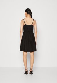 Černé šaty bez rukávů s přiléhavým živůtkem, řaseným pasem a rozšířenou sukní. Mají tenké ramínka, měkký materiál a minimalistický design.