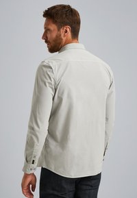 Camisa de manga larga gris claro en una tela suave con cuello abotonado, puños con botones y un diseño de dobladillo curvado.