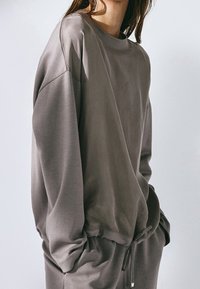 Grijze sweatshirt met een losse pasvorm, ronde hals en verlaagde schouders. Zachte stof met minimale naden en een zoomdetail met trekkoord.