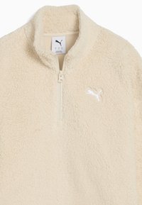 Cremefarvet fleece-pullover med høj krave, halv-zip design og et lille hvidt logo på brystet. Blødt, struktureret stof.