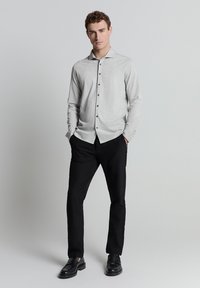 Lichtgrijze longsleeve shirt met een button-down kraag, zwarte knopen, gecombineerd met zwarte broek en zwarte instappers. Eenvoudig en stijlvol ontwerp.