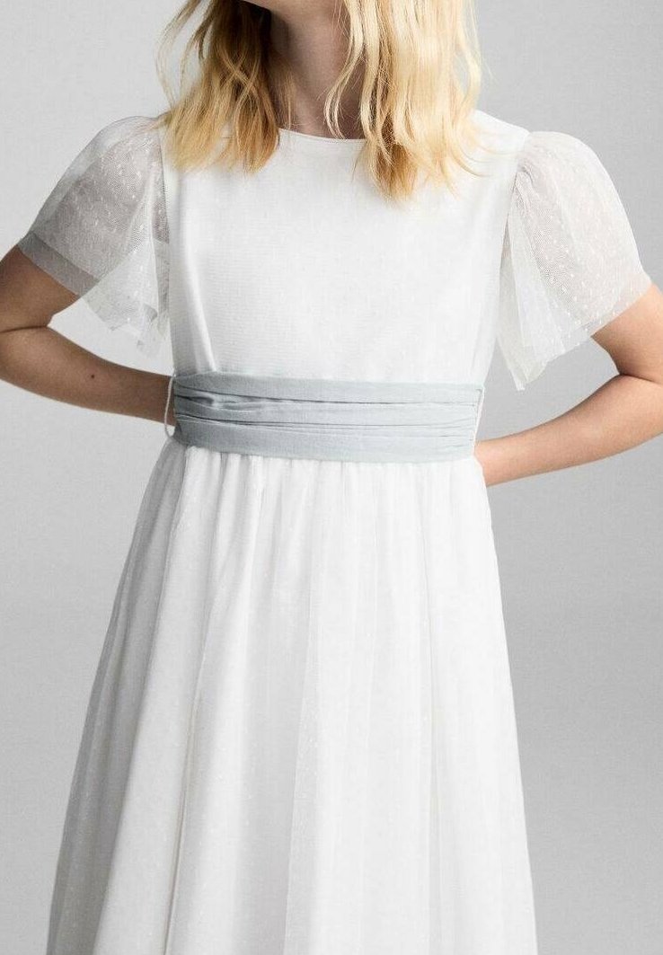Robe blanche avec manches bouffantes transparentes et une large ceinture gris argenté, portée par une personne aux cheveux blonds mi-longs.