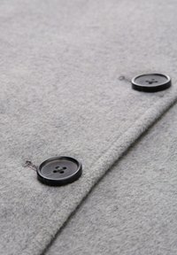 Tissu en laine grise avec une texture douce, comportant deux boutons en plastique noir et des détails de couture subtils.