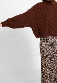 Brown cable-knit sweater with a high neckline and wide sleeves, paired with a black and tan zebra-striped skirt.