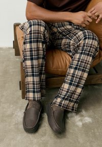 Beige en marineblauwe geruite broek van zachte stof, met een rechte pijp. Draagt met bruine leren loafers en grijze sokken.