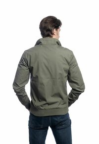 Veste vert olive avec un col haut et un ourlet élastique ; présente un tissu lisse et légèrement texturé ainsi que deux poches latérales.
