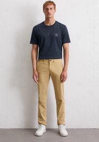 Marineblauw katoenen t-shirt met een klein logopatch, gecombineerd met beige katoenen chinos en witte sneakers. De outfit heeft een casual pasvorm.