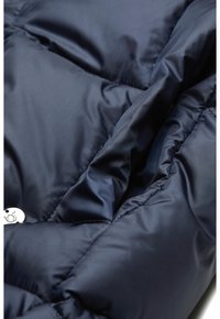 Marineblaue Steppjacke mit einem gesteppte Design, glatter Textur und metallischem Druckknopfdetail, das einen Nahaufnahm des Stoffes zeigt.