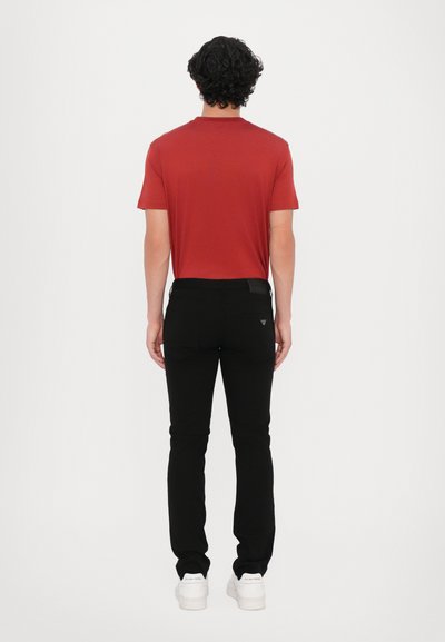 Rotes kurzärmeliges T-Shirt kombiniert mit schwarzen Slim-Fit-Hosen und weißen Sneakers. Das Shirt hat einen standardmäßigen Ausschnitt; der Stoff wirkt glatt.