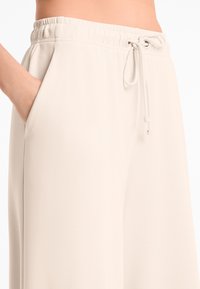 Light beige wide-leg pants with an elastic waistband, drawstring closure, and side pockets, made from soft, smooth fabric.