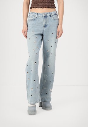 Lichtblauwe wijde jeans met meerdere ronde metalen oogjes, gedragen met grijze platformschoenen en een cropped bruin topje.