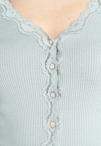 Top azzurro chiaro a coste con bordo in pizzo lungo il colletto e la placca dei bottoni, caratterizzato da bottoni rosa e un design aderente.