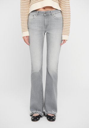 Gray flared jeans with a mid-rise waist. Features five pockets and distressed hem. Paired with black shoes with silver accents.