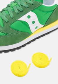 Baskets vertes en tissu avec des accents en daim, ornées d'un logo blanc et de lacets jaunes. Semelle extérieure en caoutchouc noir.