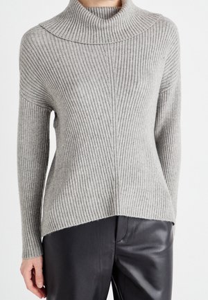 Pull en maille côtelée grise avec un col roulé ample, porté avec un pantalon en cuir noir, montrant le devant et une partie des bras.