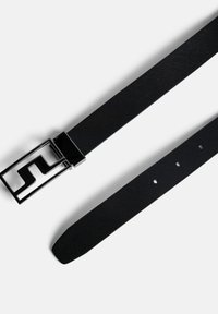 Svart bälte av strukturerad tyg med en rektangulär metallspänne som har en geometrisk design och flera justerbara hål.