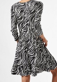 Vestido a rayas blanco y negro con mangas de tres cuartos, dobladillo con volantes y cintura ajustada, hecho de tela ligera.