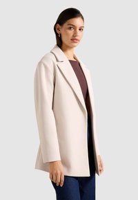 Blazer bej deschis cu rever în formă de vârf, mâneci lungi și o siluetă curată, structurată. Textură moale fără închideri vizibile.