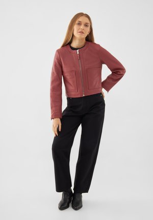 Chaqueta corta de cuero rojo con cuello redondo, cremallera frontal y dos grandes bolsillos de parche. Combinada con pantalones de pierna ancha negros y botas negras.