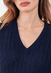 Pull en maille bleu marine avec un col en V, des bords côtelés et un motif torsadé. Texture douce avec une coupe près du cou.