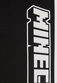 Il tessuto nero presenta grandi lettere bianche in grassetto allineate verticalmente. Il testo ha un design blocco, geometrico, con bordi netti.