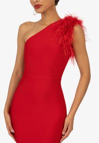 Robe rouge moulante avec un design à une épaule. Présente un accent en plumes sur l'épaule gauche. Texture lisse et tissu extensible.