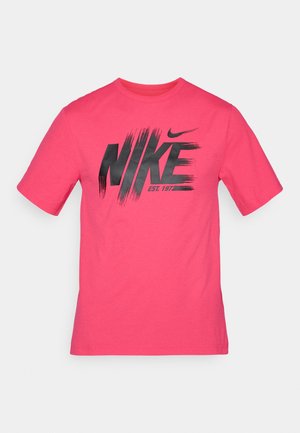 T-shirt en coton rose vif à manches courtes avec un logo Nike noir et "EST. 1977" imprimé en gras dans un style de coup de pinceau.