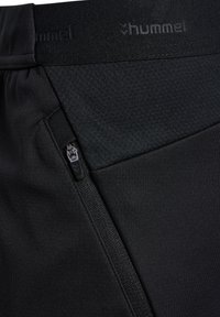 Zwarte sportbroek met een textuur, voorzien van een ritszak aan de zijkant en een gladde tailleband met de opdruk "hummel."