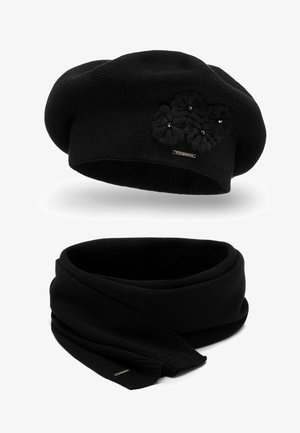 Zwarte gebreide baret met textuurflorale accenten en een gouden merketiket. Bijpassende zwarte gebreide sjaal, plat met taps toelopende uiteinden en een zachte afwerking.