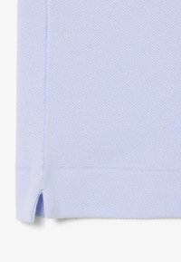 Tissu bleu clair texturé avec un motif subtil, présentant une coupe droite et des fentes latérales à l'ourlet pour faciliter les mouvements et le confort.