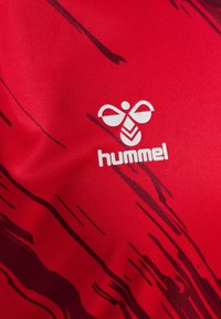 Röd sporttröja med mjuk textur, med abstrakta svarta randmönster och en vit "hummel"-logotyp nära mitten.