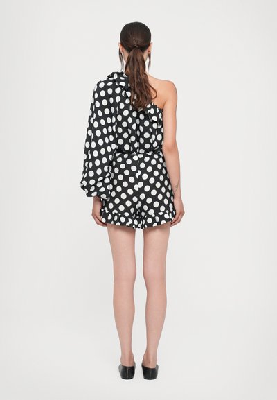 Schwarzer und weißer Polka-Dot-Overall mit einem rüschengeschmückten langen Ärmel. Verfügt über ein tailliertes Oberteil und Shorts mit einem rüschierten Saum. Glatte Stoffstruktur.